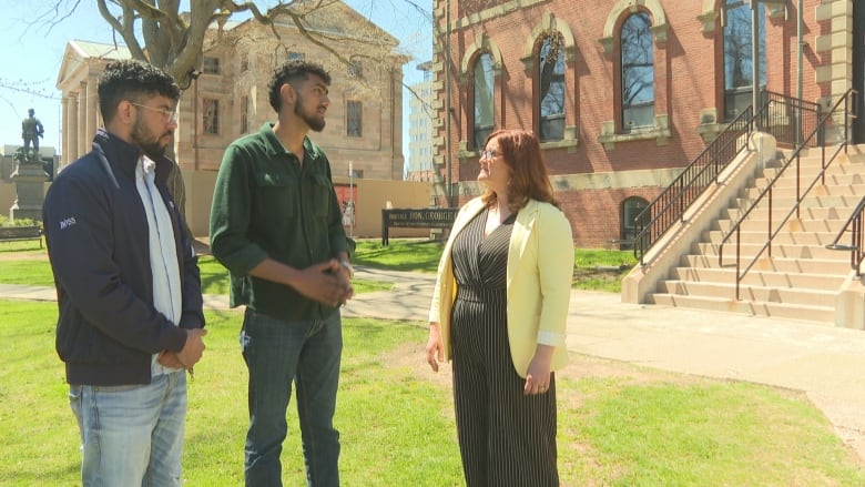 Two men speaking with woman on lawn.