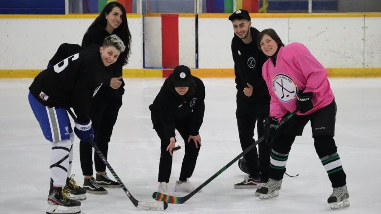 Two hockey players and three organizers stand on a hockey rink