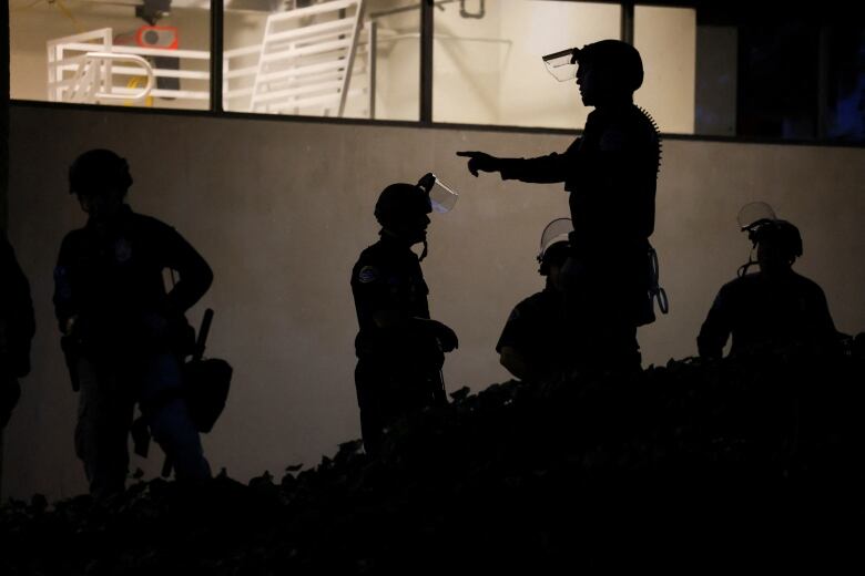 Police officers appear in silhouette beside illuminated windows of a building.