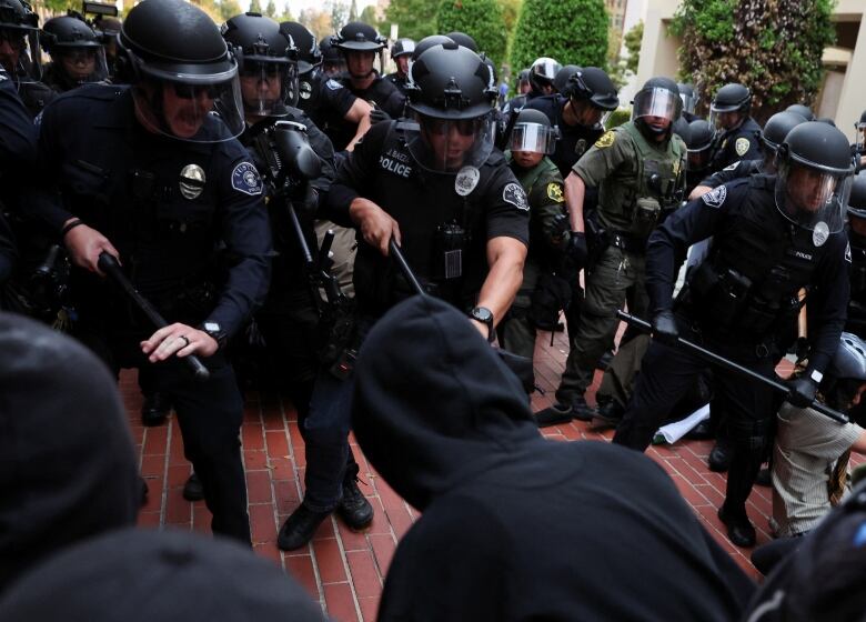 Officers wearing face shields and carrying batons, confront protesters.