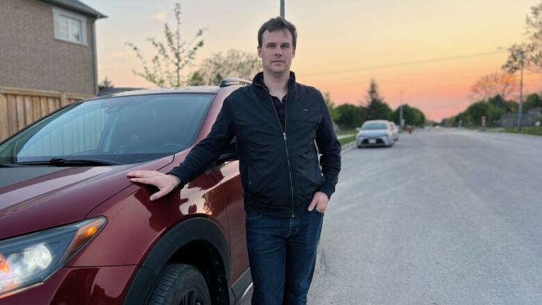 A person stands outside by a red car.