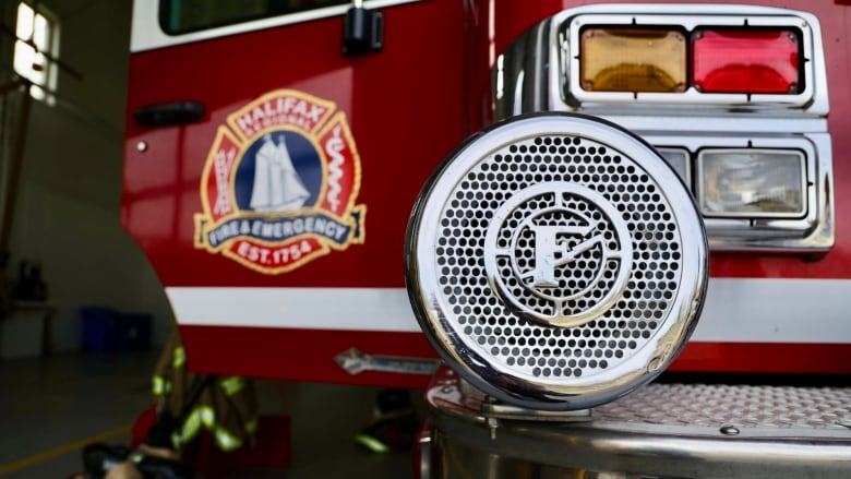 A close up of a chrome siren on the front of a red fire engine. The passenger door is open and says 