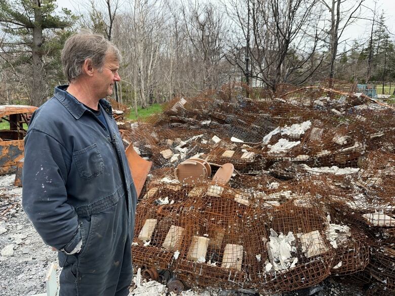 A man in blue coveralls is shown by lobster traps that were burned and mangled in the Shelburne County wildfire.