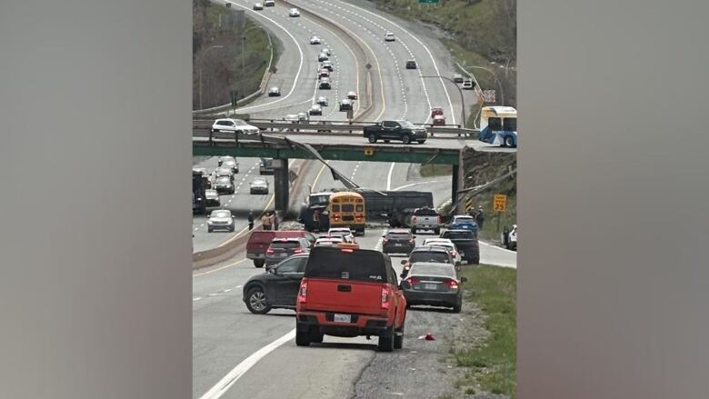 Cars lined up on a highway near a tractor trailer that fell from an overpass.