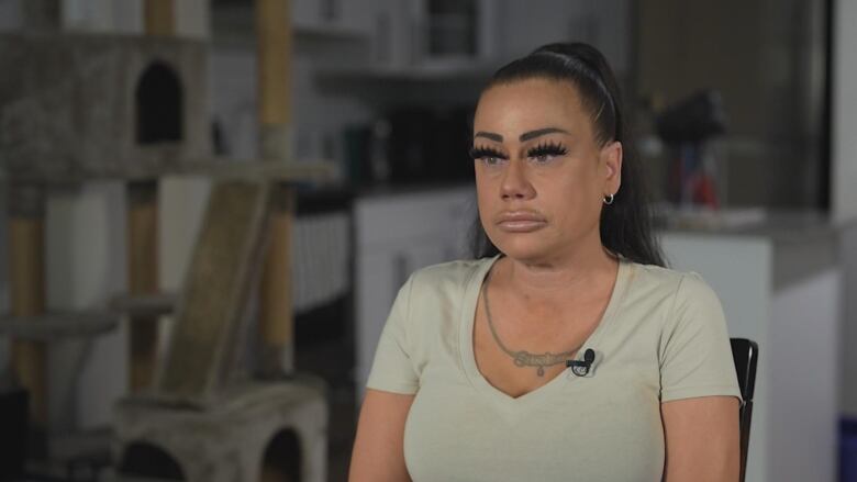 A woman sits in her living room looking sad/serious.