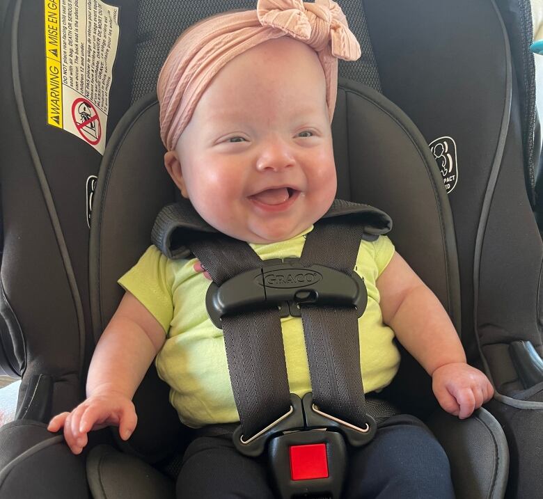 A baby smiles while strapped into a car seat. 