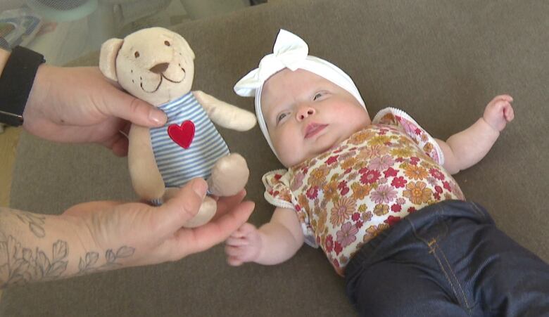 Sutton lays on the couch, reaching for her teddy bear.