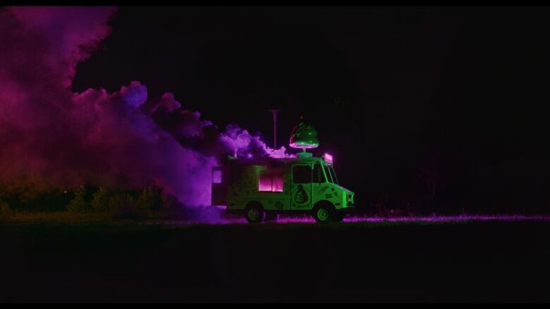 An ice cream bus has glowing purple smoke billowing out of it. It is night time.