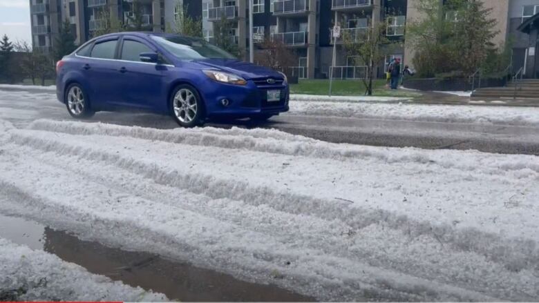 A car drives past hailstones piled several centimetres deep.