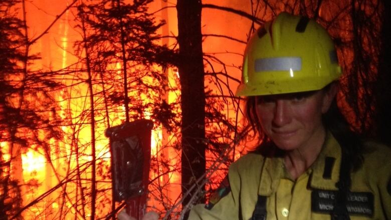 A woman in firefighting gear is seen against a blazing wildfire.