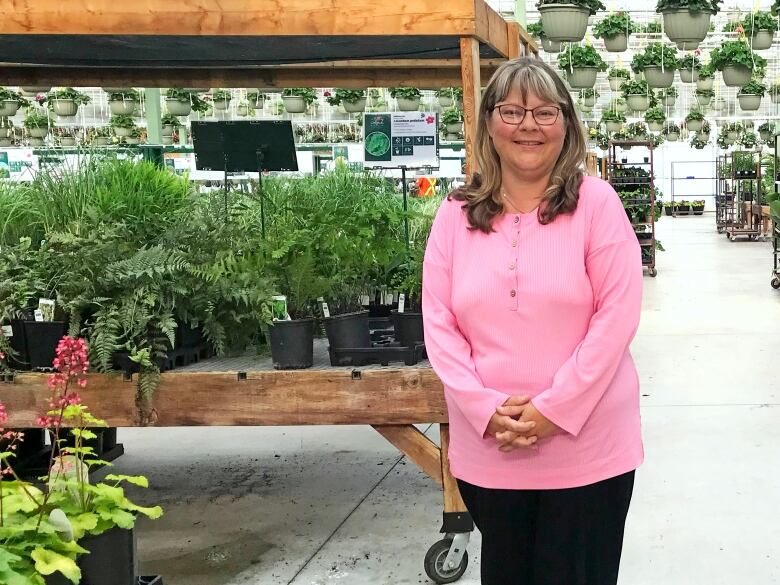 A woman wearing a bright pink shirt stands in front of a display of fruits and vegetables for gardening.