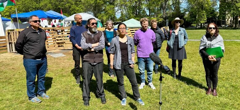 Nine people stand on the grass in front of an encampment