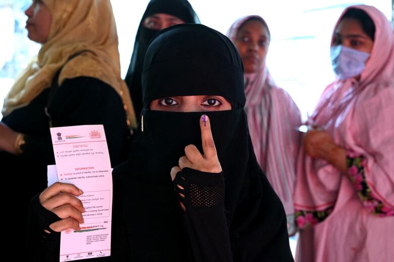 A woman shows off her inked finger. She holds a voting ballot in her right hand.