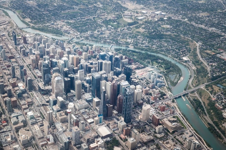 A view from the air of downtown skyscrapers on the left, next to winding river. On the right are neighbourhoods with trees.