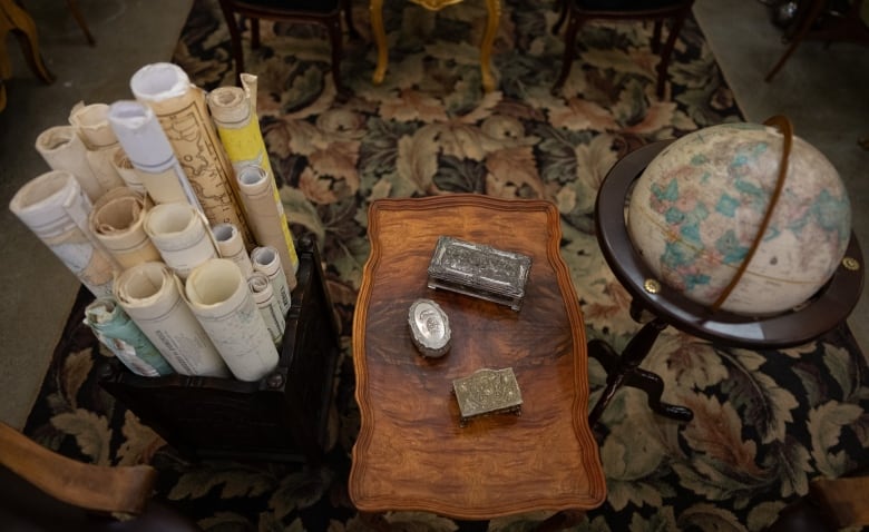 a collection of rolled maps, jewelry boxes and a globe sit on an antique table and rug