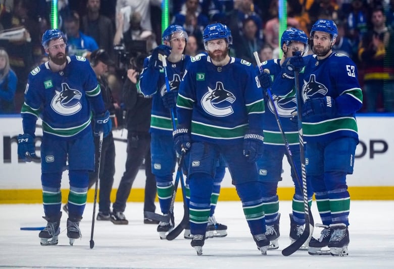 A group of hockey players wearing blue look dejected on the ice.