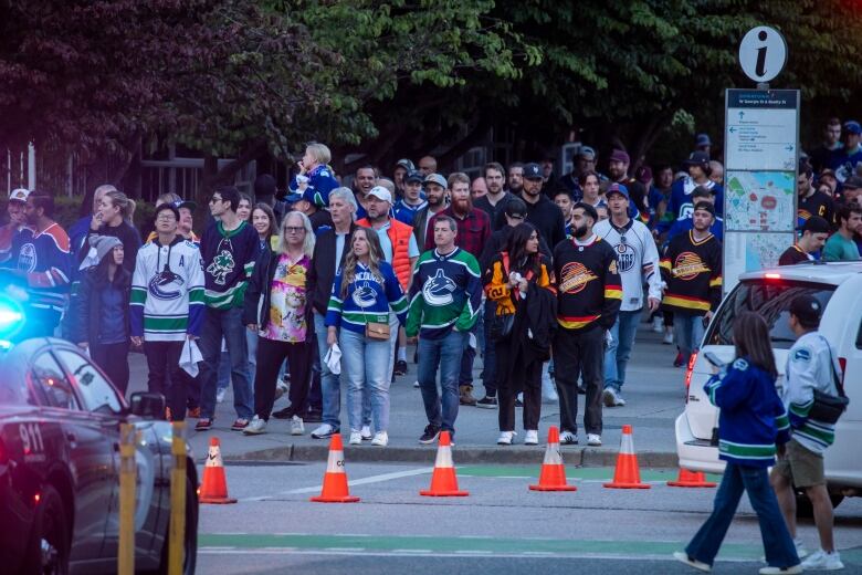 A gaggle of hockey fans crowd a busy city street.