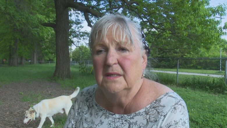 A senior-age woman in a park with a dog in the background.