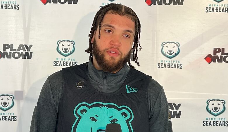 A man with braided hair wears a basketball jersey with a polar bear image