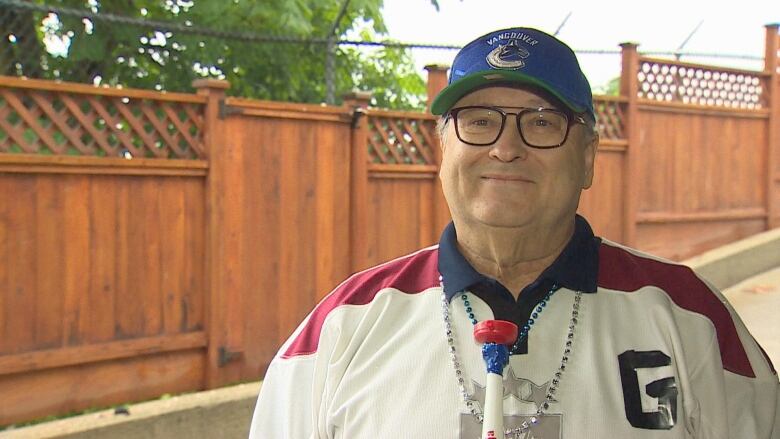 A bespectacled man wearing a white and red jersey and a Vancouver Canucks baseball cap. 