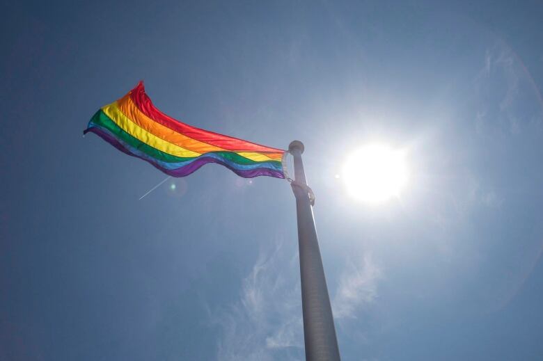 A rainbow flag flies with a blue sky in the background. 