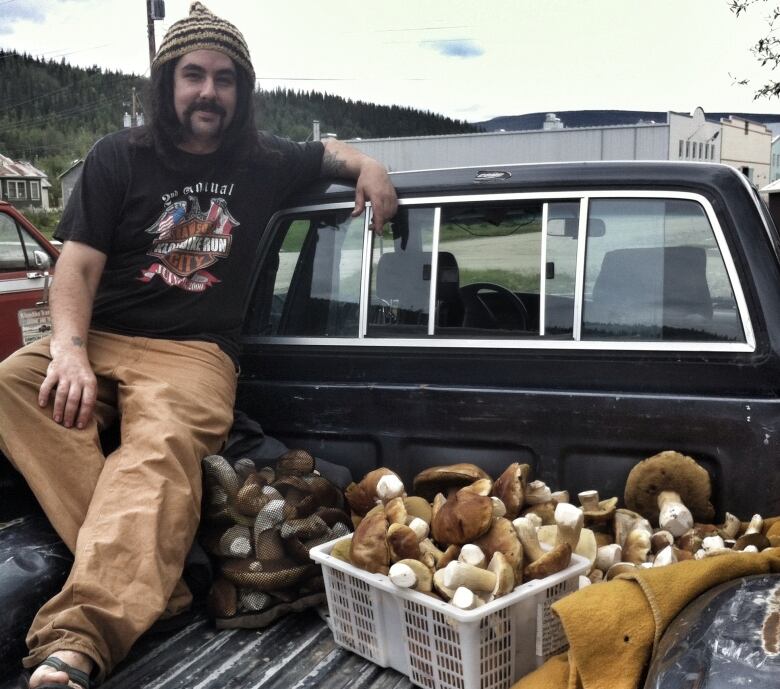 A man sitting on the back of his truck with mushrooms.