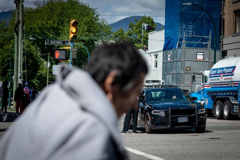 A man in a grey hoodie walks in front of a Vancouver Police Department cruiser in the Downtown Eastside neighbourhood of Vancouver.