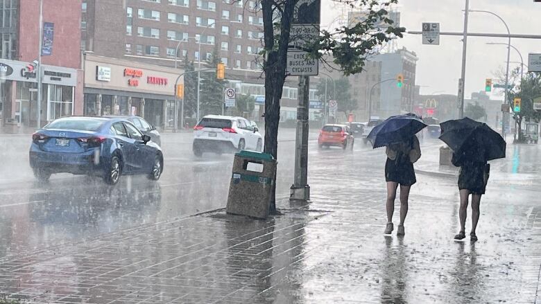 Two people with umbrellas walk down a city street in heavy rainfall.