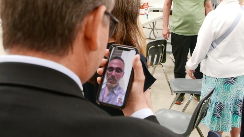 A man holds a phone and speaks to another man by video chat.