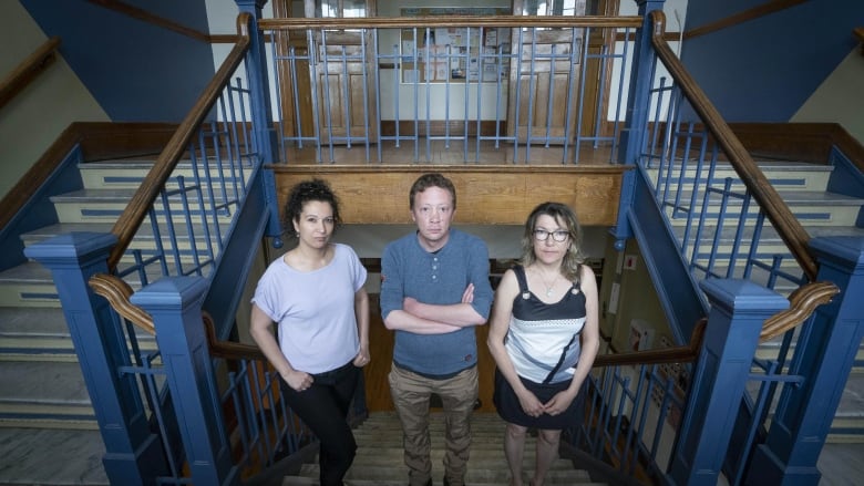 Three people standing in a staircase inside a large community centre. 