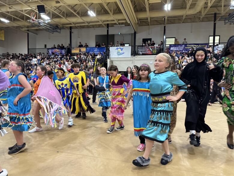 A group of children wearing colourful Indigenous clothing dance in a gymnasium.