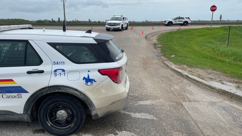 Three RCMP vehicles are parked on a stretch of highway. Orange pylons can be seen in the background. 