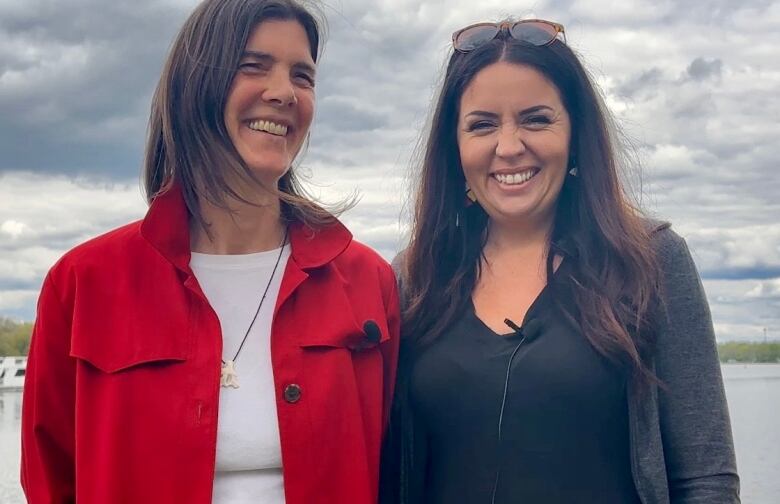 Women smile with lake behind them.