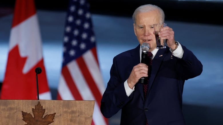 Biden raises a glass for a toast in front of a Canadian and American flag