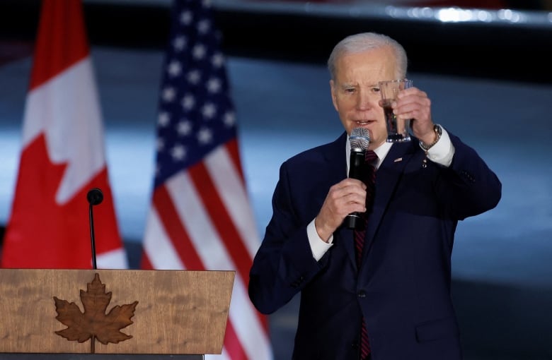 Biden raises a glass for a toast in front of a Canadian and American flag