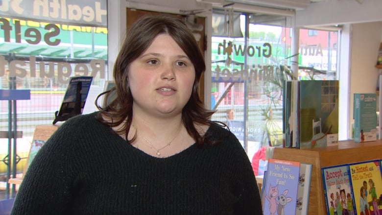 A white woman wearing a black sweater speaks in a bookshop.