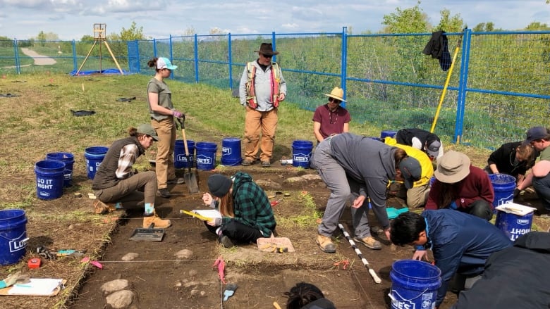 People gather around an area where dirt and rocks have been exposed in a field. 