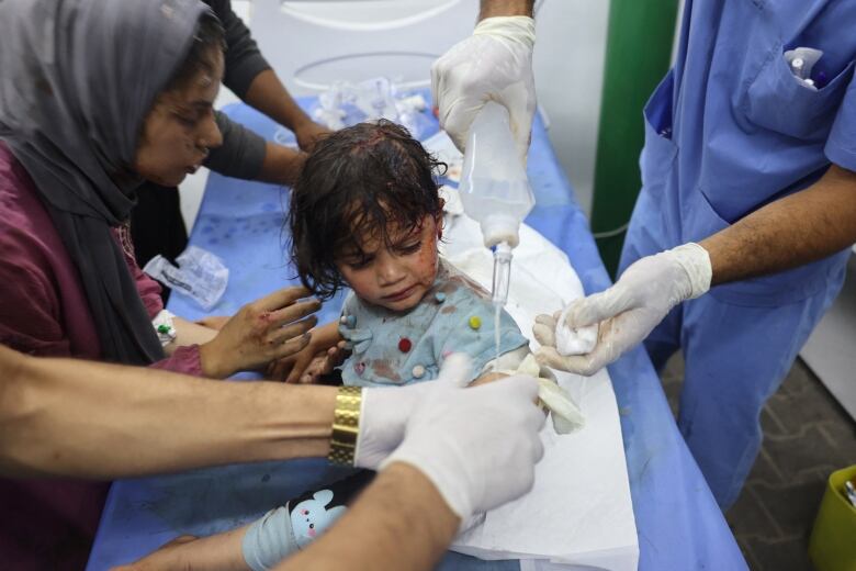 A wounded child is treated by medics and adults at a hospital. 