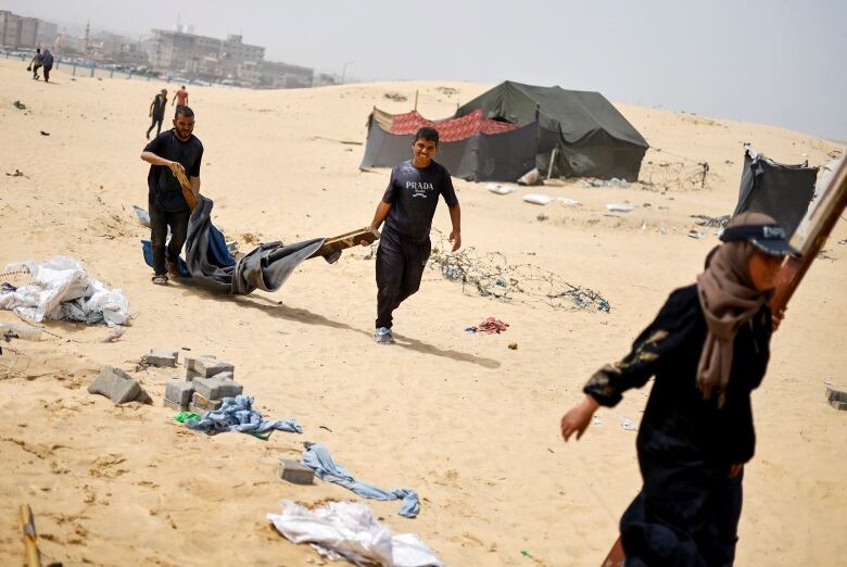 Two men and a women are shown walking on a sandy area while carrying items.