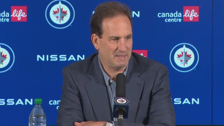 A man in a suit sits at a desk with a microphone