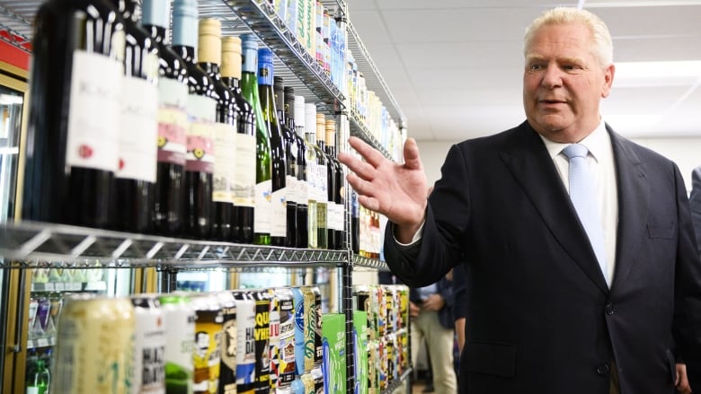 Premier Doug Ford gestures toward wine bottles on shelves. 