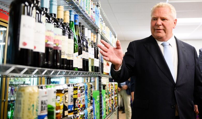 Premier Doug Ford gestures toward wine bottles on shelves. 