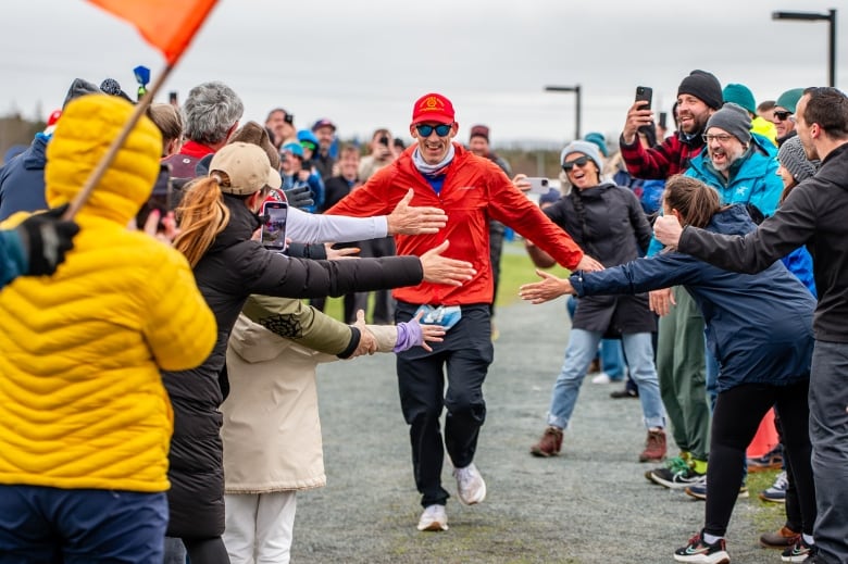 A man wearing a red jacket and red hat crossing the finish line at a running event surrounded by onlookers. 