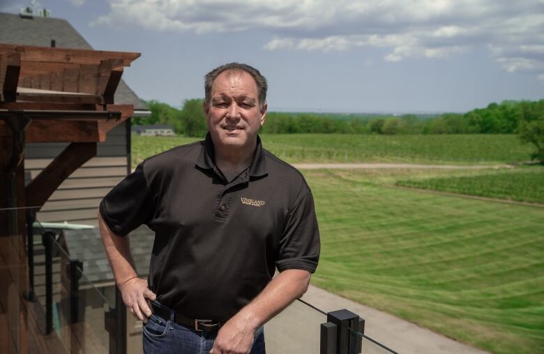 A brown-haired man wearing a black golf shirt leans on the balcony overlooking acres of vineyards. May 23, 2024. 