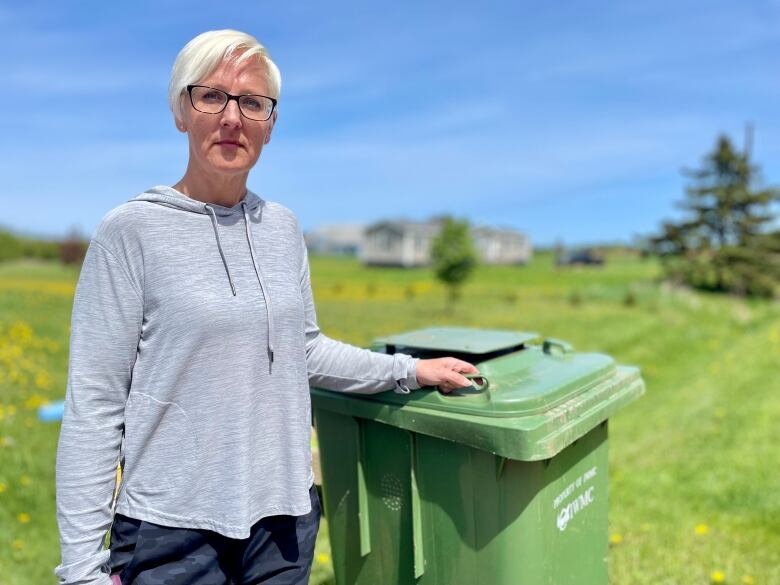 Woman standing beside green garbage bin.