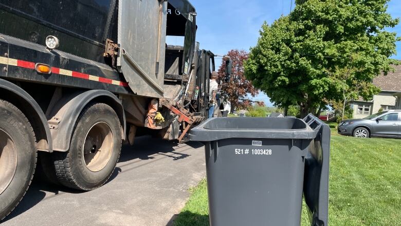 Garbage truck beside empty black bin.