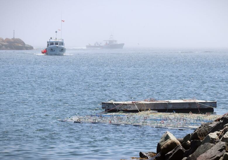 Two fishing boats emerge from fog in the distance while plastic crates tied together by colourful ropes float on the water in the foreground.