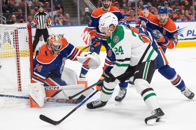 A hockey player in white and green is stopped by a goaltender in blue and orange. 