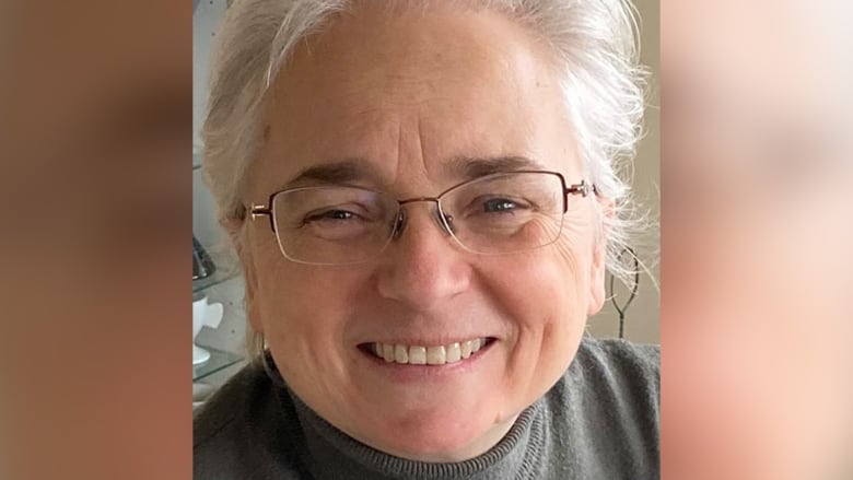 A white woman with white hair and glasses smiles.