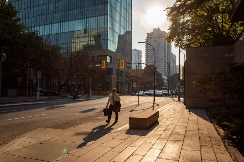 A man in a suit carries a briefcase as he walks to work downtown on a sunny morning.